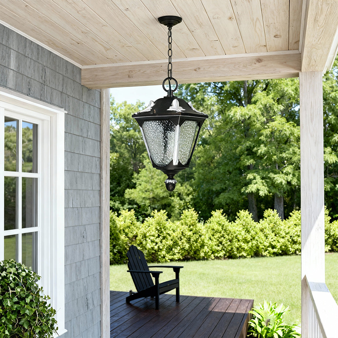 Elegant outdoor porch pendant light suspended from covered entry with blue-grey siding and greenery