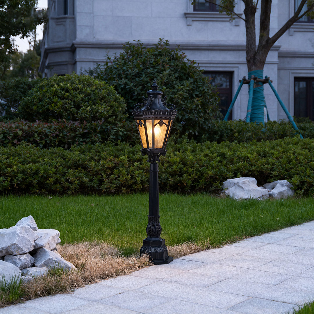 Elegant pathway lighting bollard casting warm glow on concrete path with green lawn and shrubs
