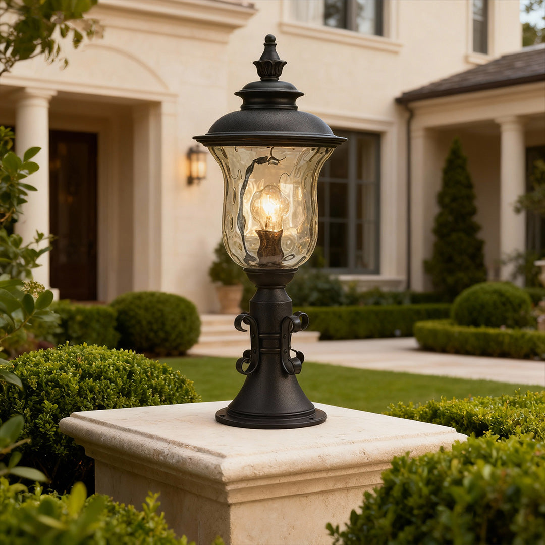 Elegant pillar gate light standing on beige pier near Mediterranean home entrance with manicured hedges