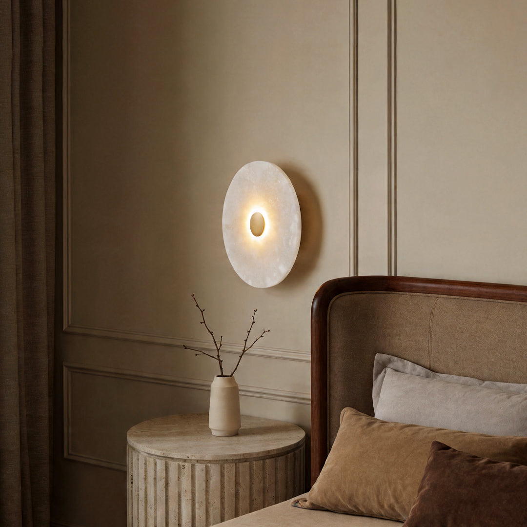 Elegant round wall light glowing on a classic paneled bedroom wall above a cozy bedside table.