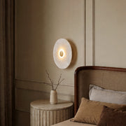 Elegant round wall light glowing on a classic paneled bedroom wall above a cozy bedside table.