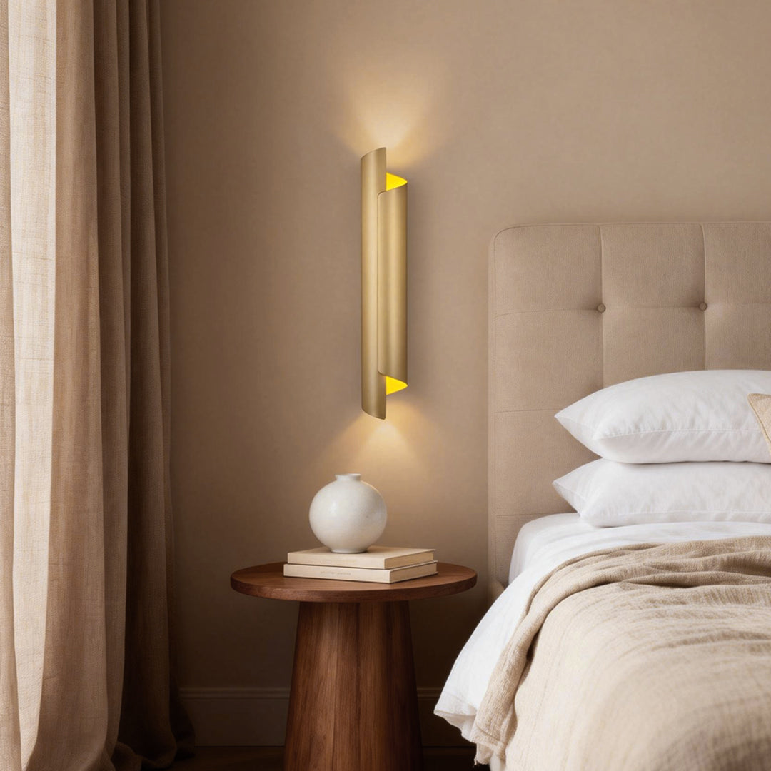 Elegant scroll wall sconce with gold accents, illuminating a cozy bedside table and decorative vase.