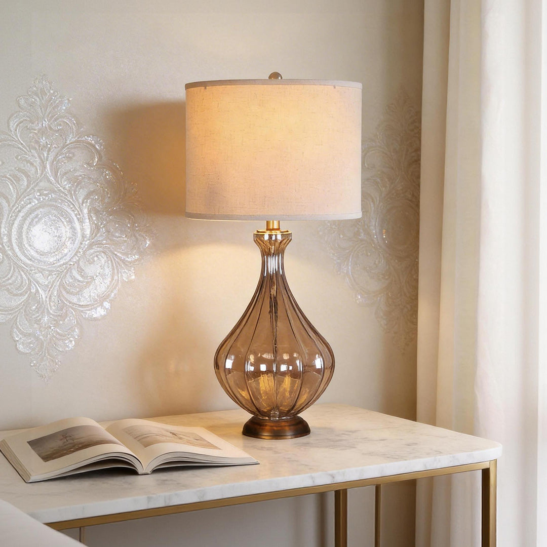 Elegant glass base table lamp with smoky ribbed texture and linen drum shade on marble consoles.