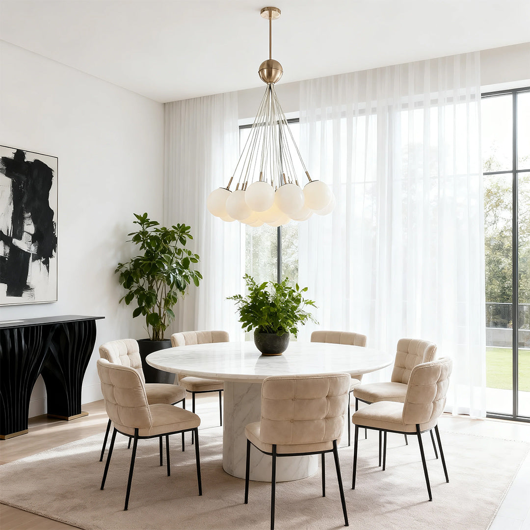 Elegant bubble glass chandelier providing soft ambient light over a round white dining table with velvet seating and sheer curtains.