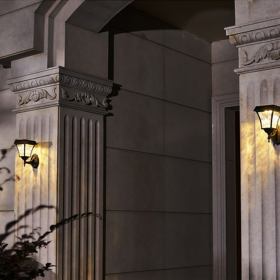 Elegant solar outdoor sconce lights providing warm accent lighting on classical architectural columns at night.