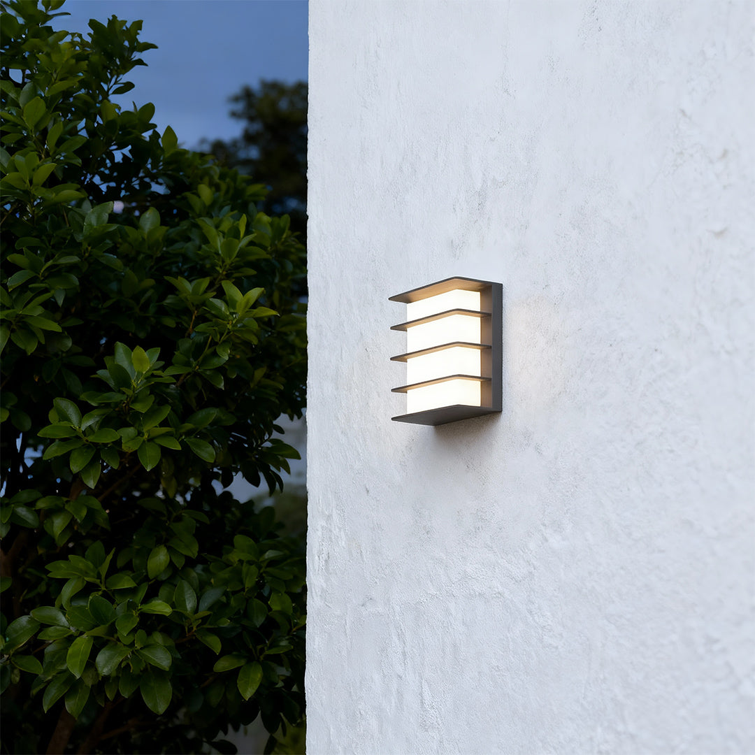 Elegant square LED wall lights with glass shade chandelier design illuminating modern light blue exterior wall at dusk.