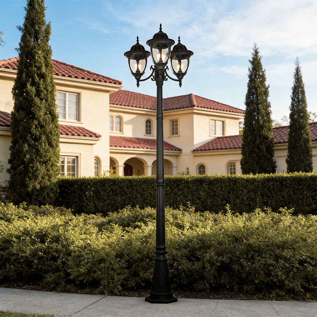 Elegant triple-head street lamp post light on a sidewalk in front of a luxury white villas.