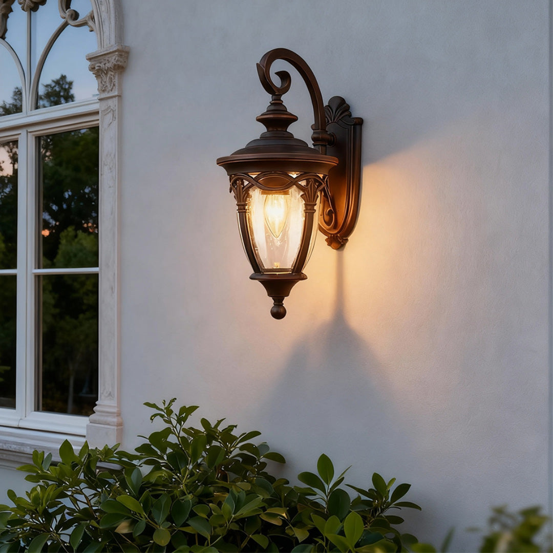 Elegant unique outdoor sconce illuminating white exterior wall near window at dusk with shrubs
