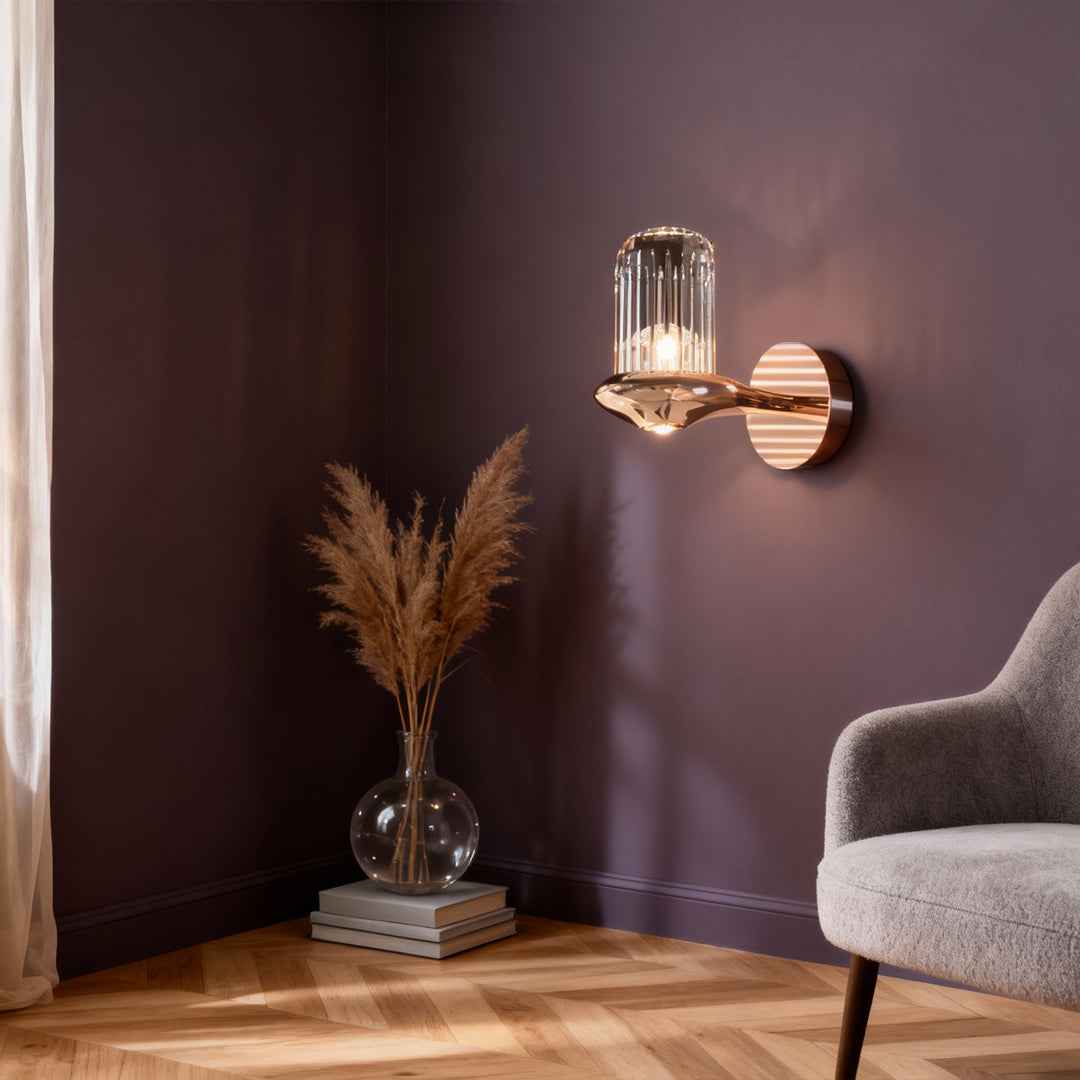 Elegant wall lights with crystals illuminating plum-colored wall beside modern armchair with decorative pampas grass