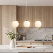 Elegant trio of White Faux Pendant Light globes over a modern marble island with wood cabinets.