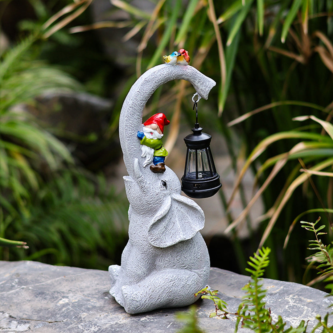 Decorative elephant lantern holder with bird accent piece displayed in natural garden environment