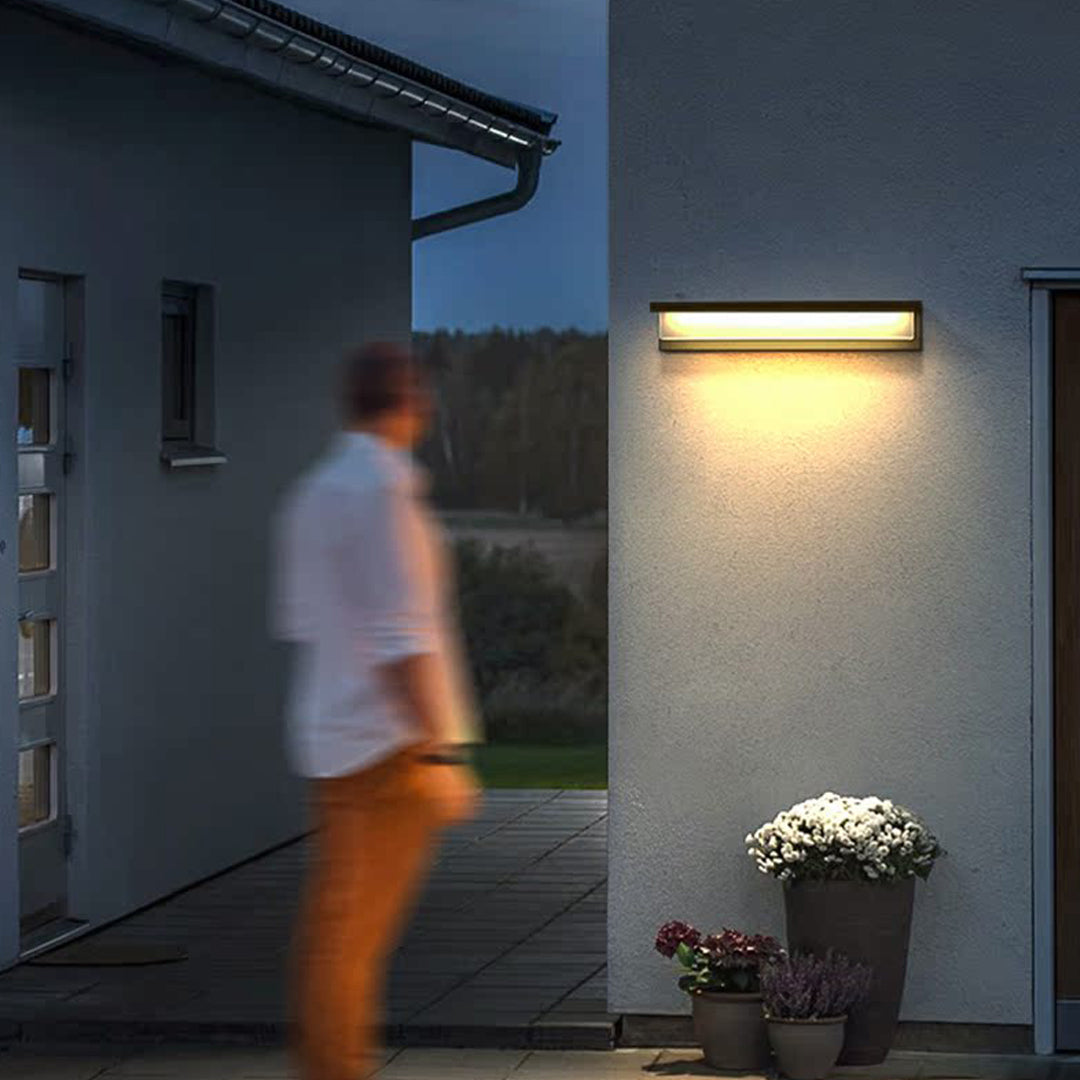 Outdoor wall sconce light fixtures casting warm light beside a modern house walkway during evening time.