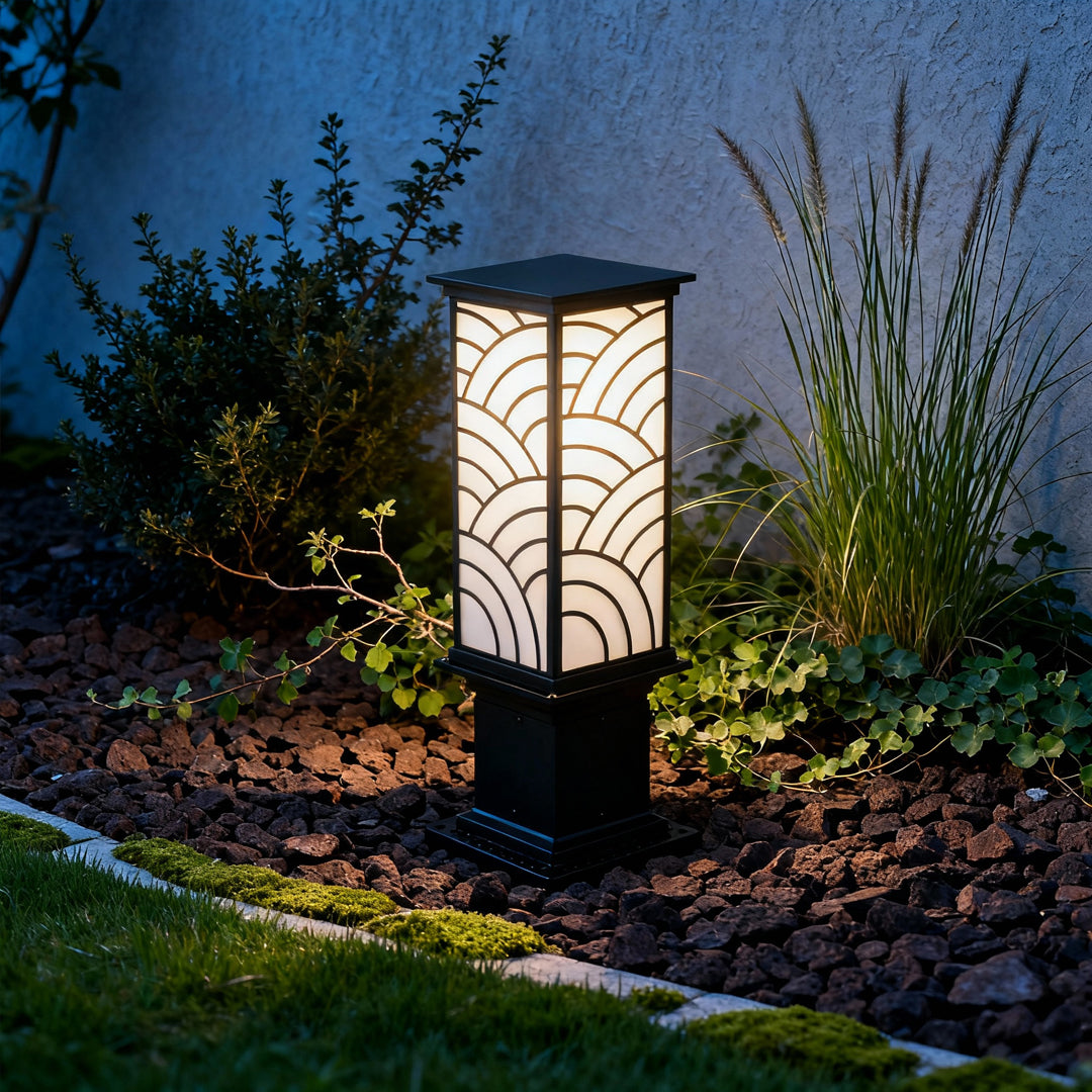 Exterior bollard light set beside greenery near a building, softly lighting the surrounding garden area.