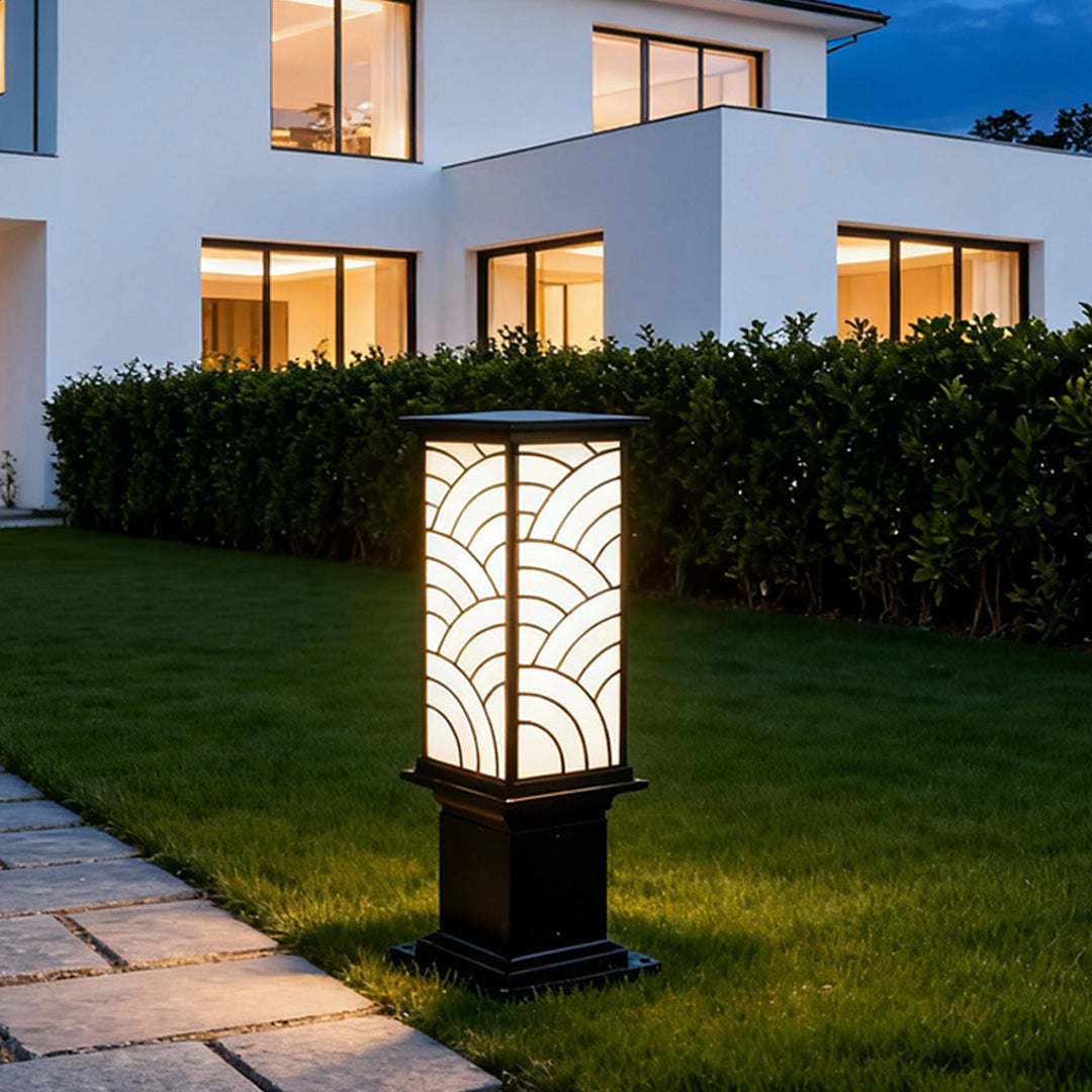 Exterior bollard light installed near a modern home entrance, adding warm glow to the surrounding shrubs and pathway.