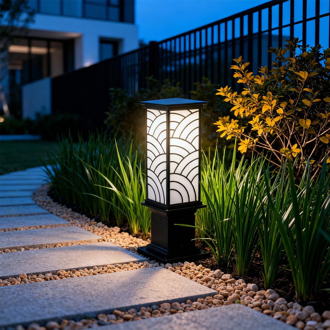 Exterior bollard light installed beside a residential fence, illuminating the outdoor pathway with warm ambient lighting.