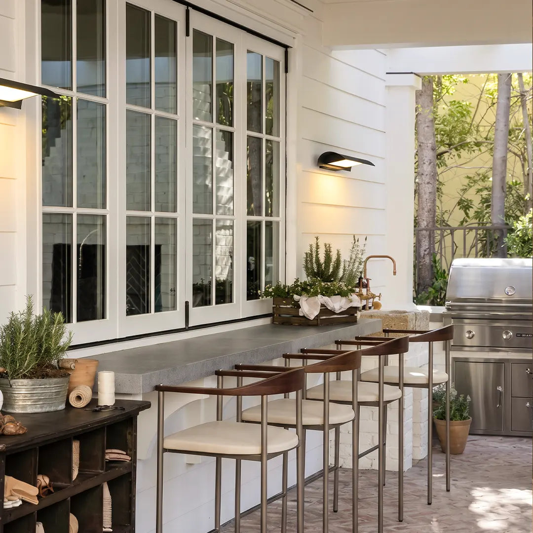 Exterior down wall lights installed along a covered outdoor kitchen wall above a patio counter with bar seating.
