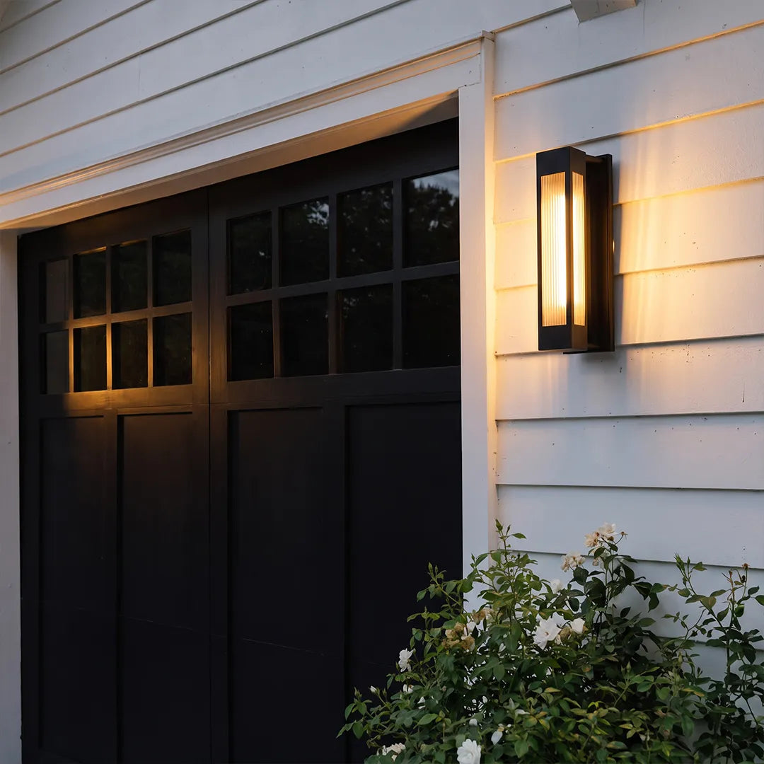 Exterior LED wall sconce lighting mounted beside a black garage door on a white modern home exterior.