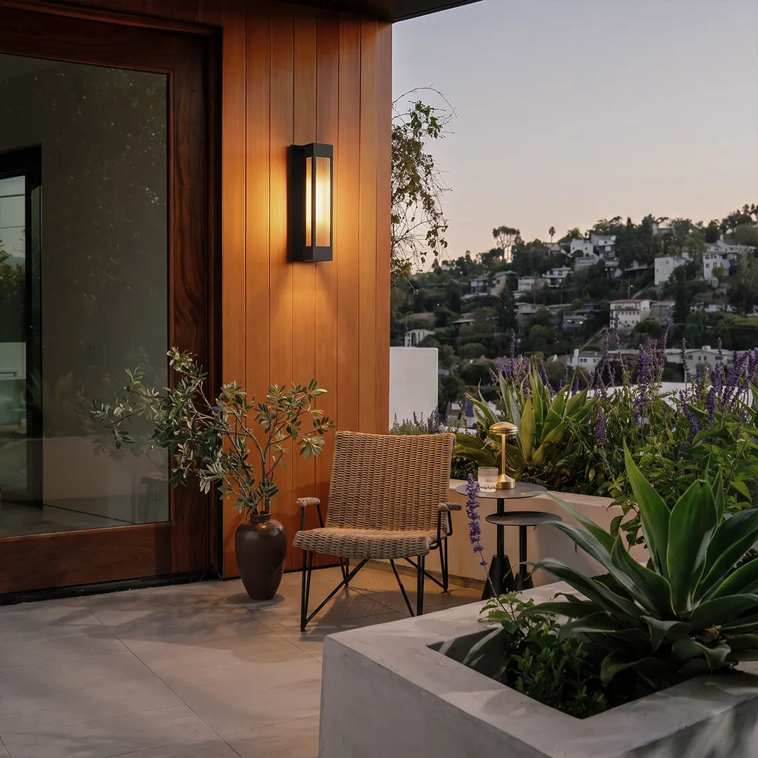 Exterior LED wall sconce lighting mounted beside a wood entry door on a modern patio with landscape views.