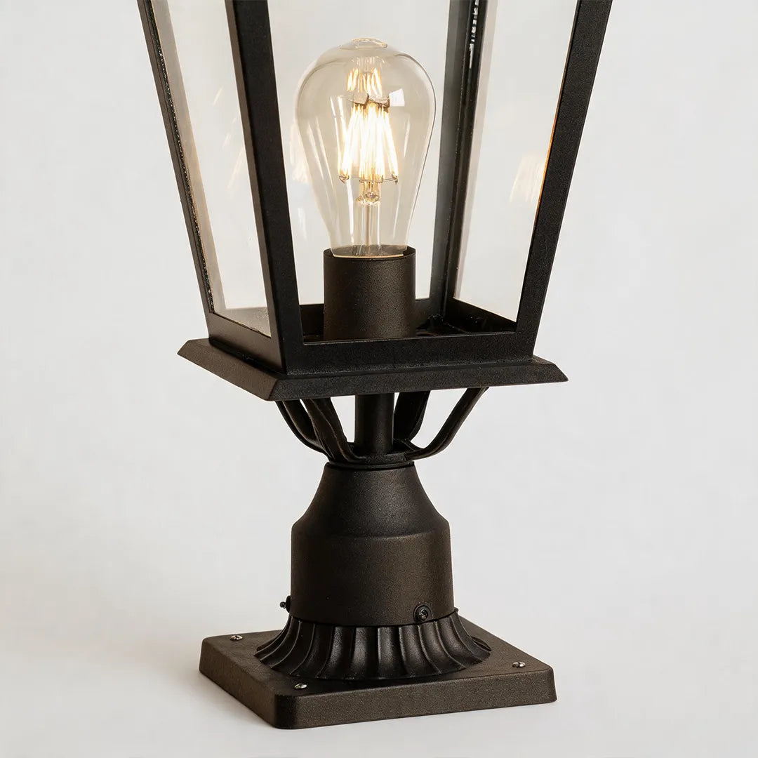 Exterior pillar light close-up showing the clear glass panels, lantern frame, and exposed bulb inside the fixture.