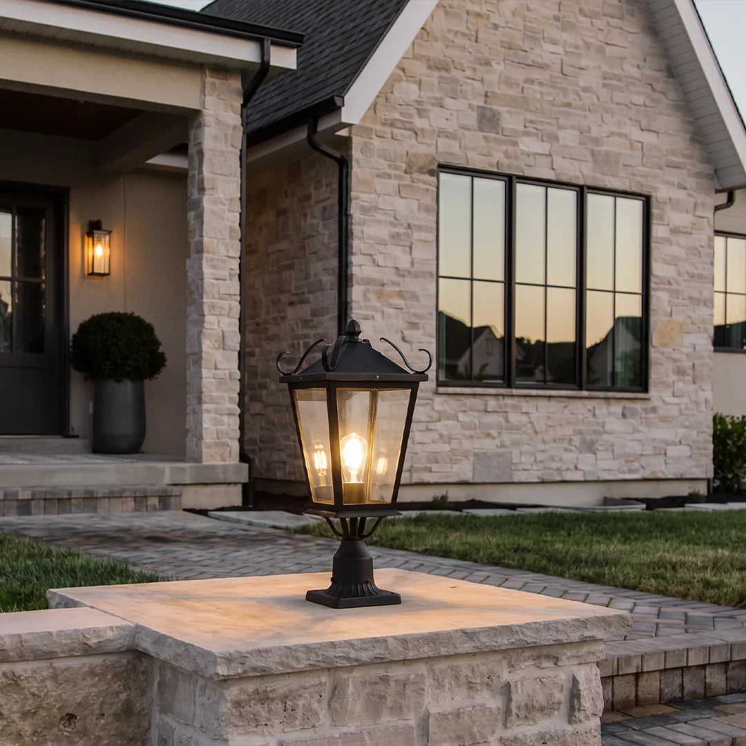 Exterior pillar light placed on a stone entry column outside a modern house, featuring a traditional lantern-inspired design.