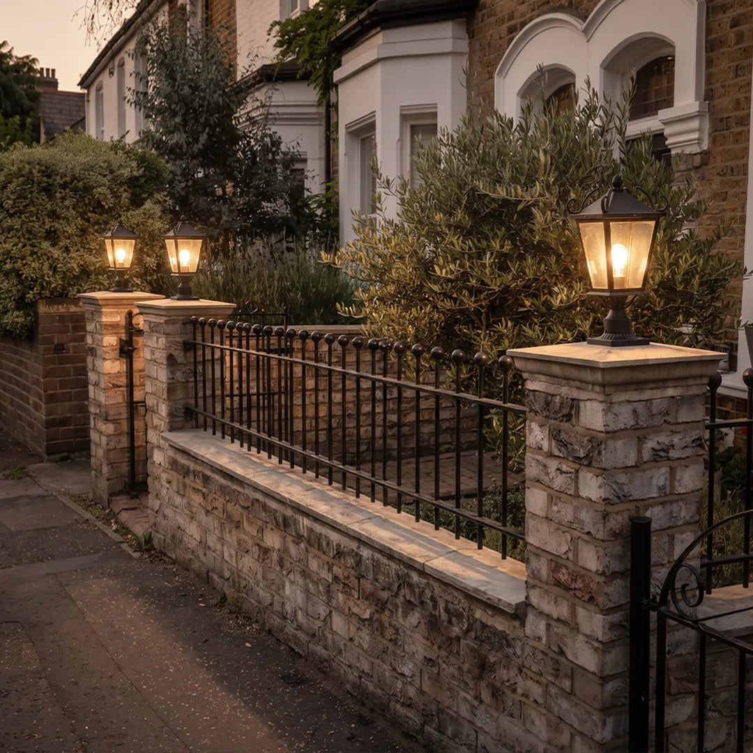 Exterior pillar lights lining a brick fence wall, providing warm lantern-style lighting along the front yard boundary.
