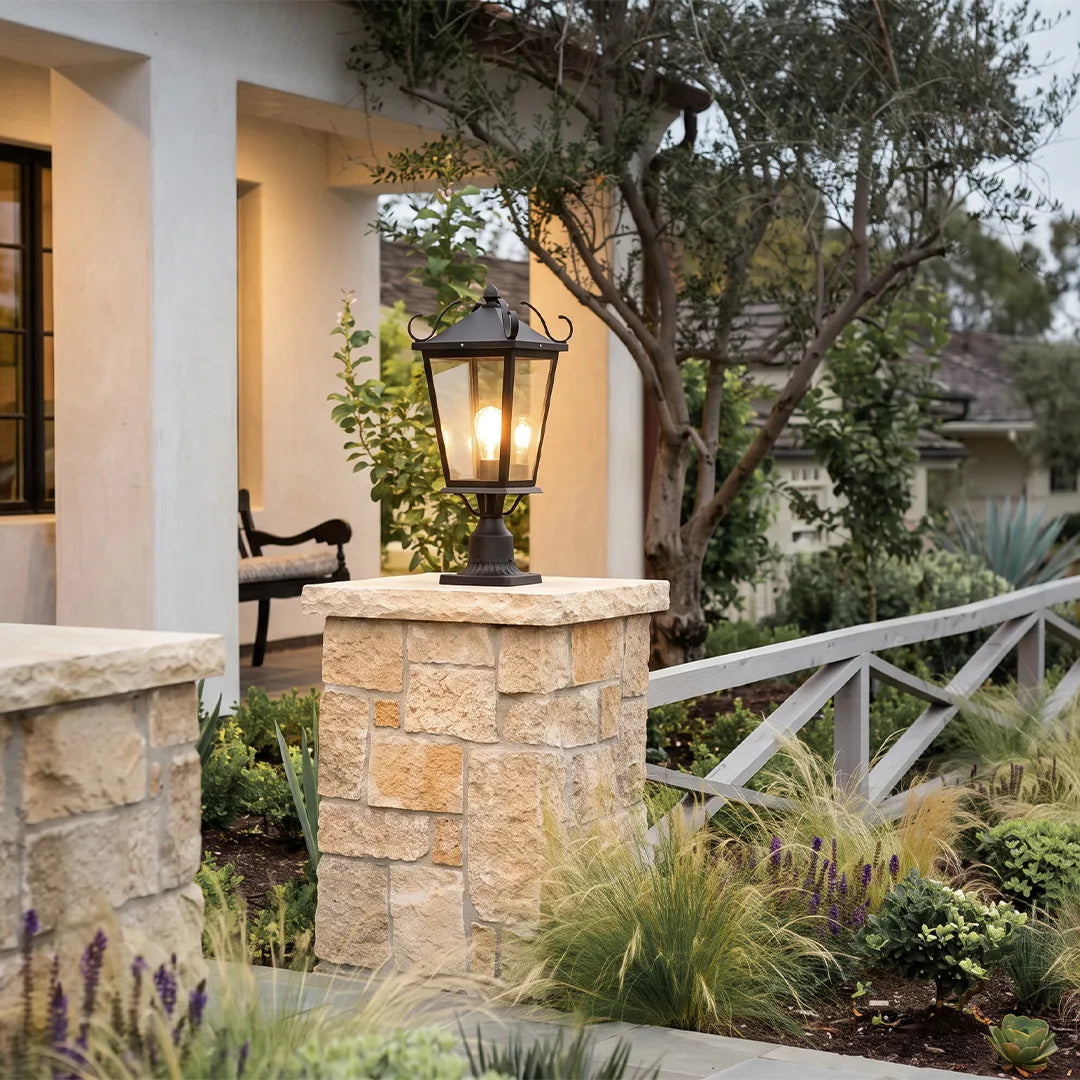 Exterior pillar lights mounted on stone gate columns beside a garden walkway, adding classic lantern-style illumination to the entrance.