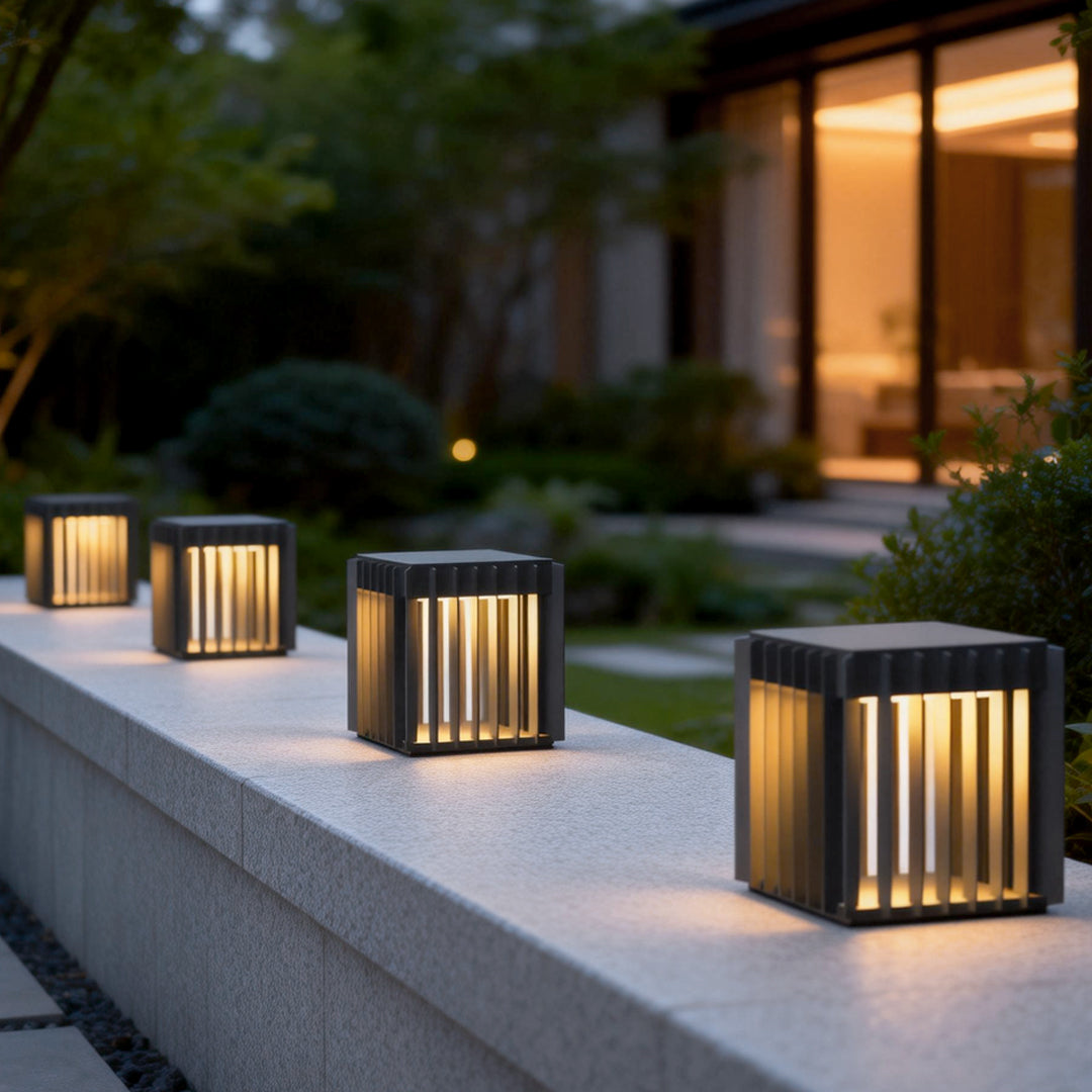 Exterior pillar lights casting a warm glow on a garden pathway with stone pillars.
