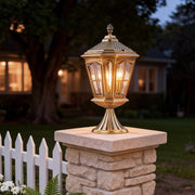 Exterior pillar mount lights casting a warm glow on a brick pillar in a cozy garden setting.