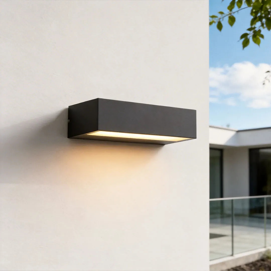 Exterior porch light fixture with a slim black rectangular frame casting warm downward light on a white wall.