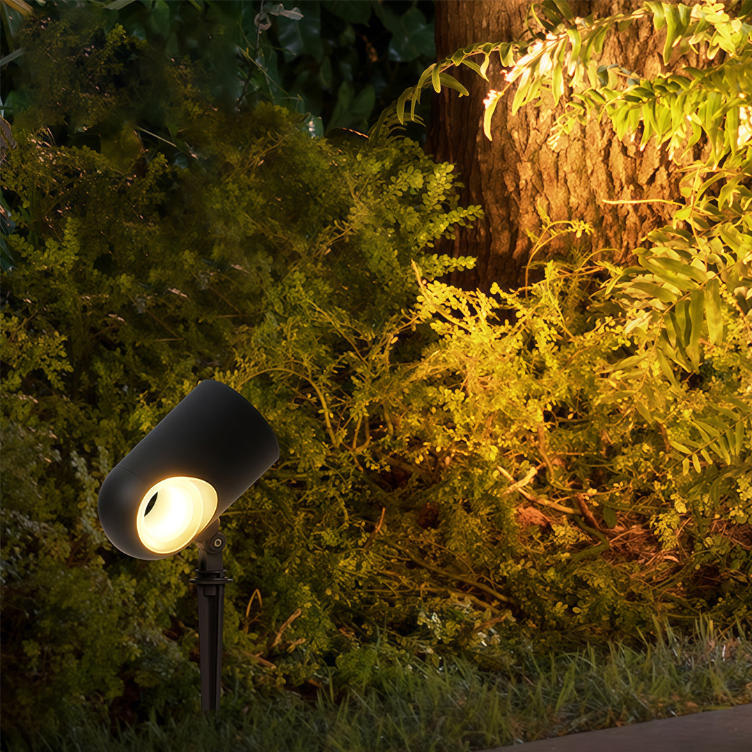 Warm beam from exterior spotlight fixtures illuminating dense garden foliage during nighttime.