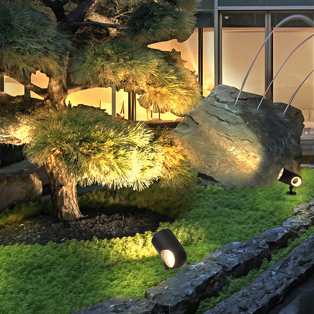 Exterior spotlight fixtures lighting a landscaped yard with soft warm beams along stone pathways.