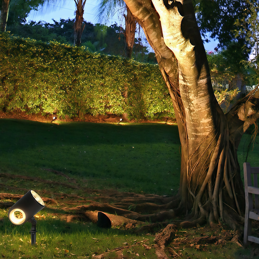 Subtle warm-toned exterior spotlight fixtures illuminating outdoor greenery in a residential garden.