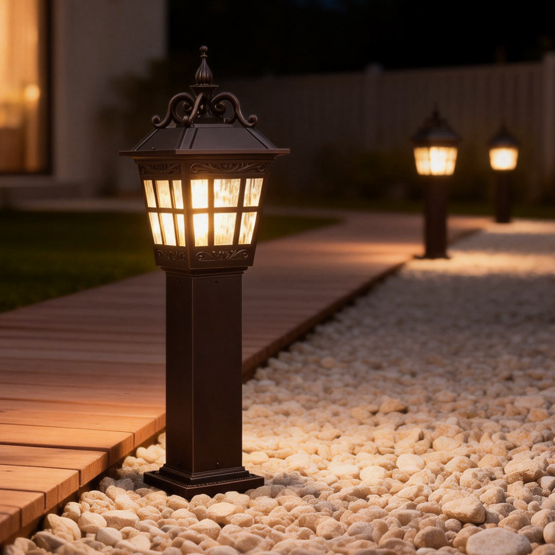 External post lights casting a soft glow on a garden pathway with white pebbles.