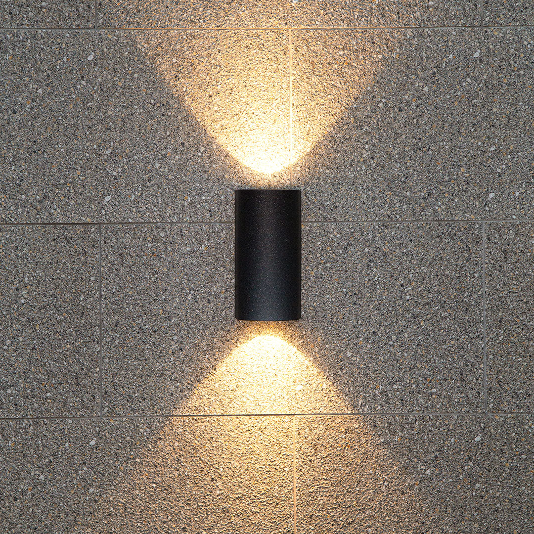Modern black outdoor light producing brilliant warm illumination against rich textured wall