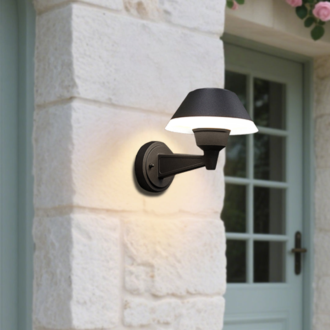 Contemporary outdoor wall sconce with conical shade casting warm light on white siding