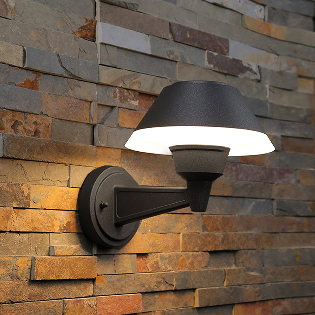 Contemporary outdoor wall sconce with conical shade casting warm light on white siding