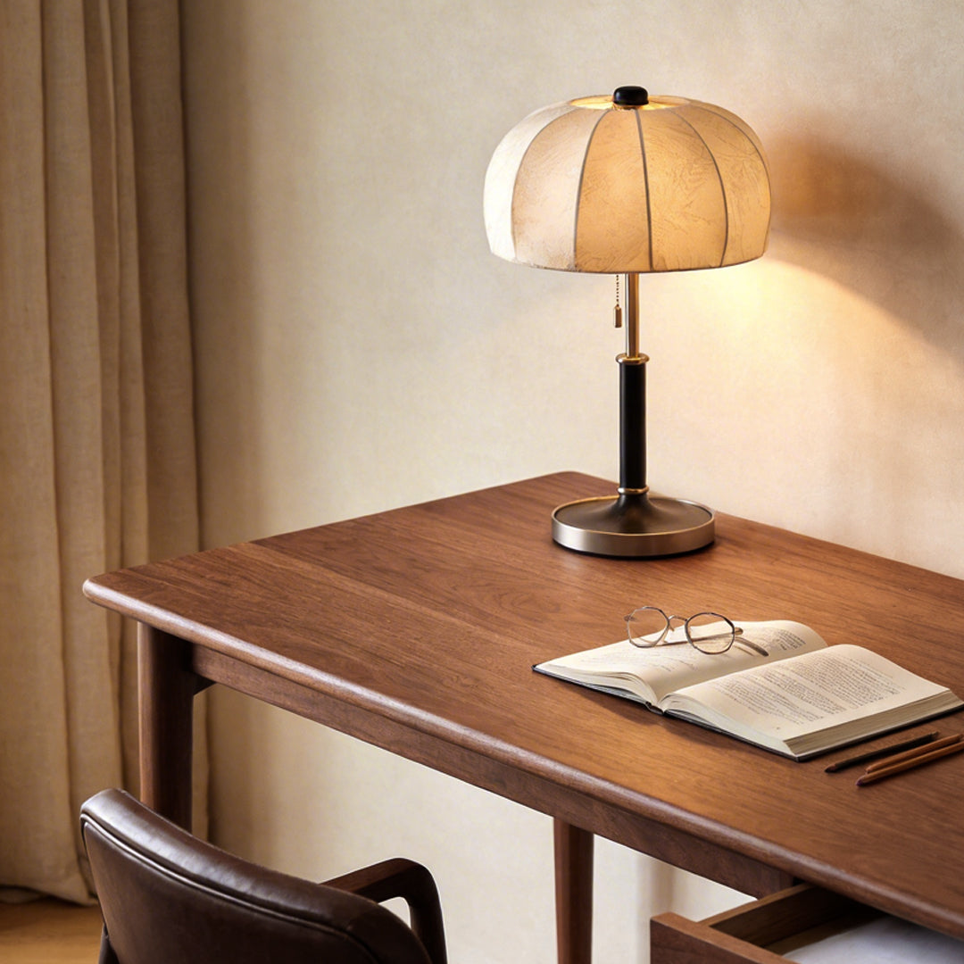 Fabric table lamp with a beige fabric shade, providing warm light on a wooden desk.