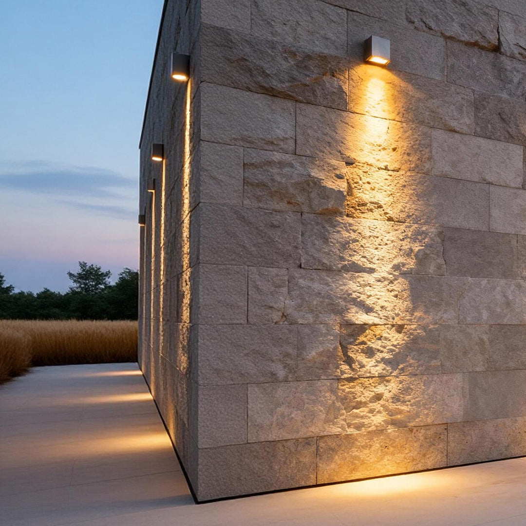 Facade spot lights mounted along a building corner, creating dramatic uplighting on textured stone surfaces at dusk.