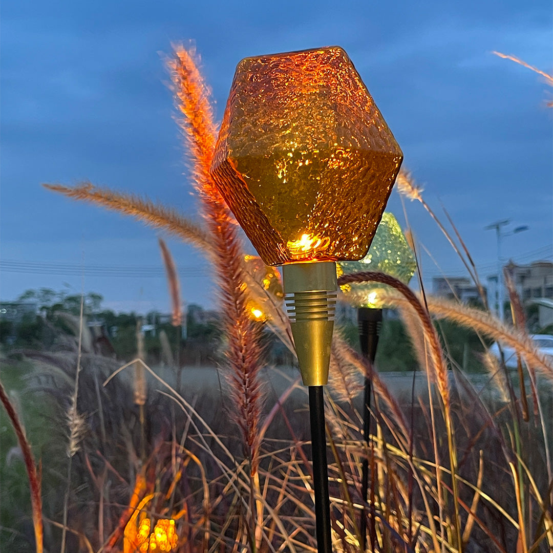 Faceted amber globe stake casting patterned light for decorative outdoor landscape lighting pathway.