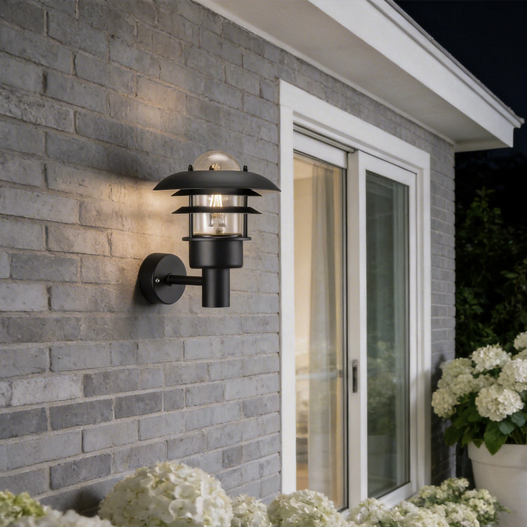 Farmhouse outdoor sconce with a classic black design, mounted beside a brick house entrance.