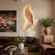 Feather wall lamp above a brown leather sofa, featuring a sculptural feather shape with warm ambient backlighting.