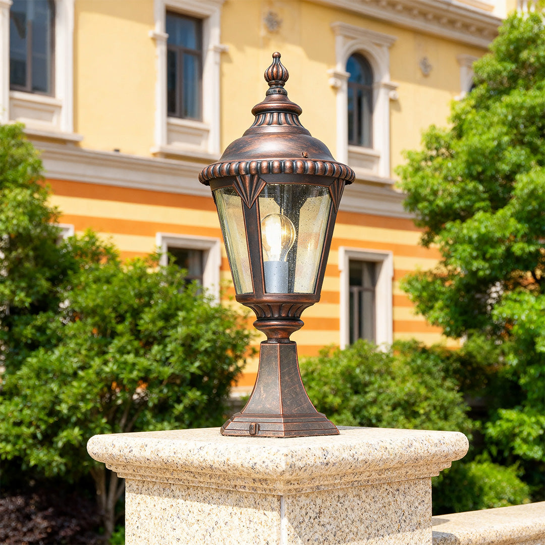 Fence pillar light mounted on stone fountain edge with yellow building and greenery backdrop