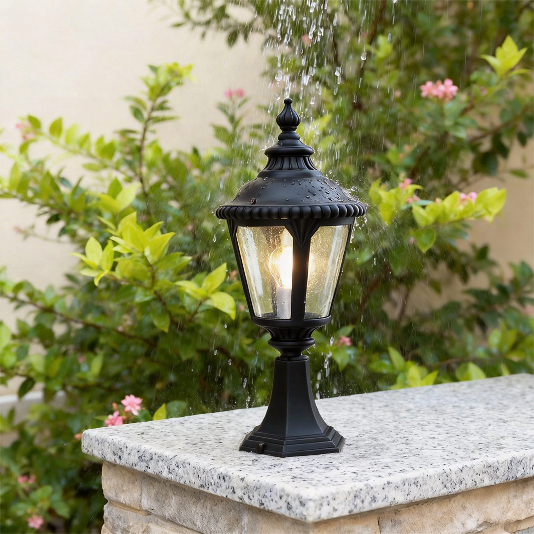 Fence pillar lights placed on a concrete fence post surrounded by green shrubs and flowers.