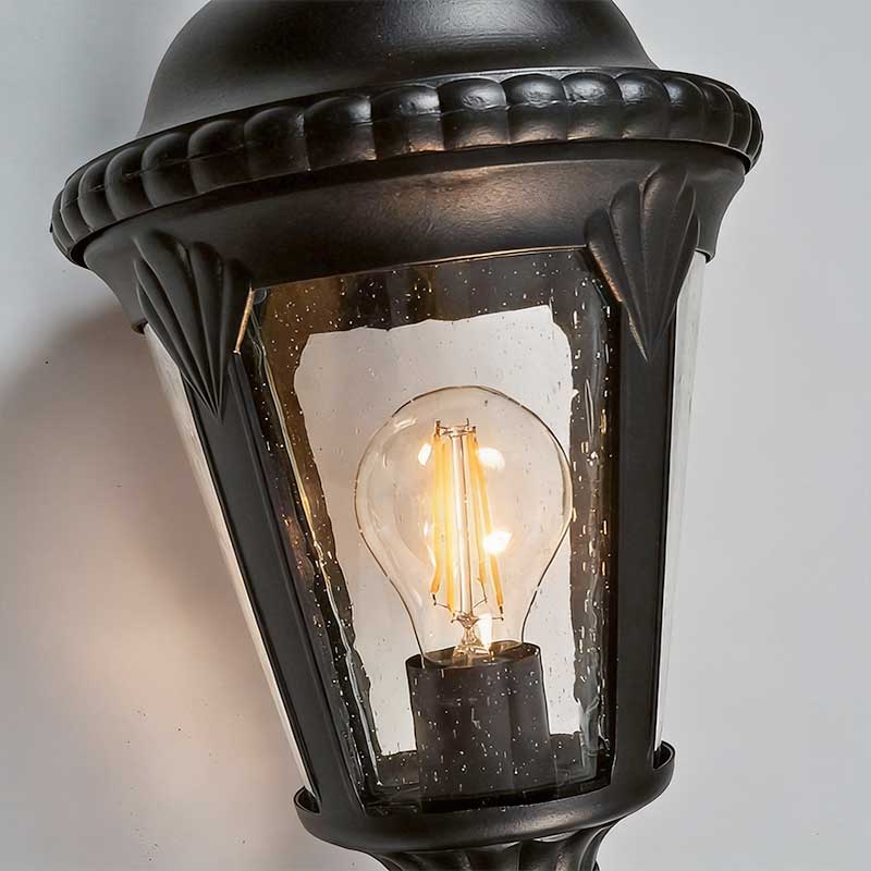 Fence pillar lights detail showing the lantern body, clear seeded glass, and exposed bulb inside.