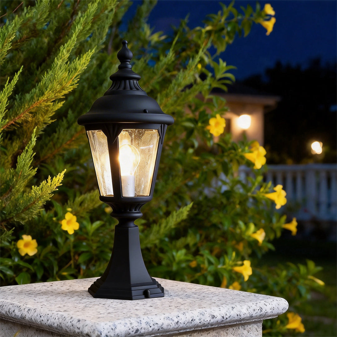 Fence pillar lights glowing at night on a stone post near yellow flowers and garden greenery.
