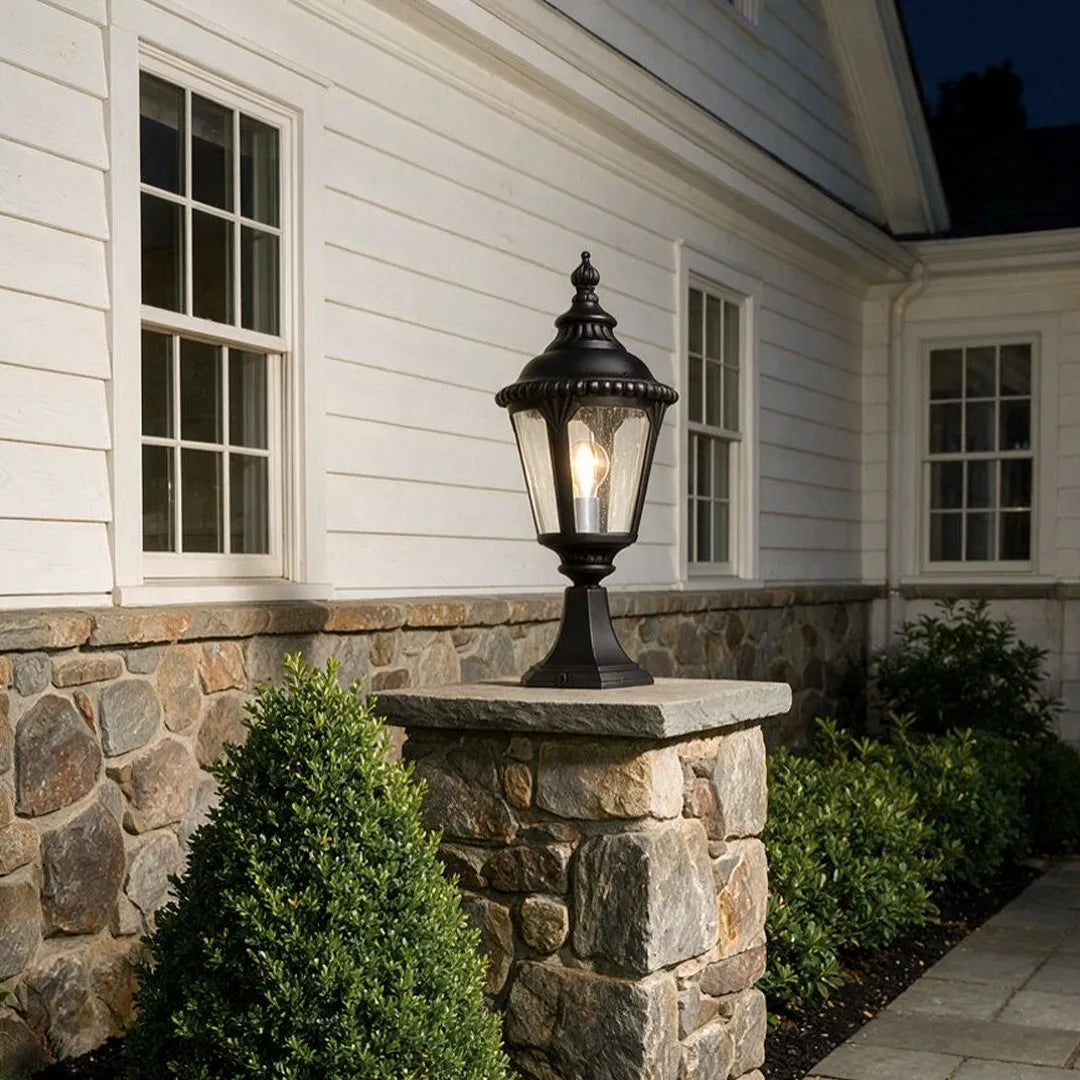 Fence pillar lights mounted on a stone gate post beside a white house exterior.