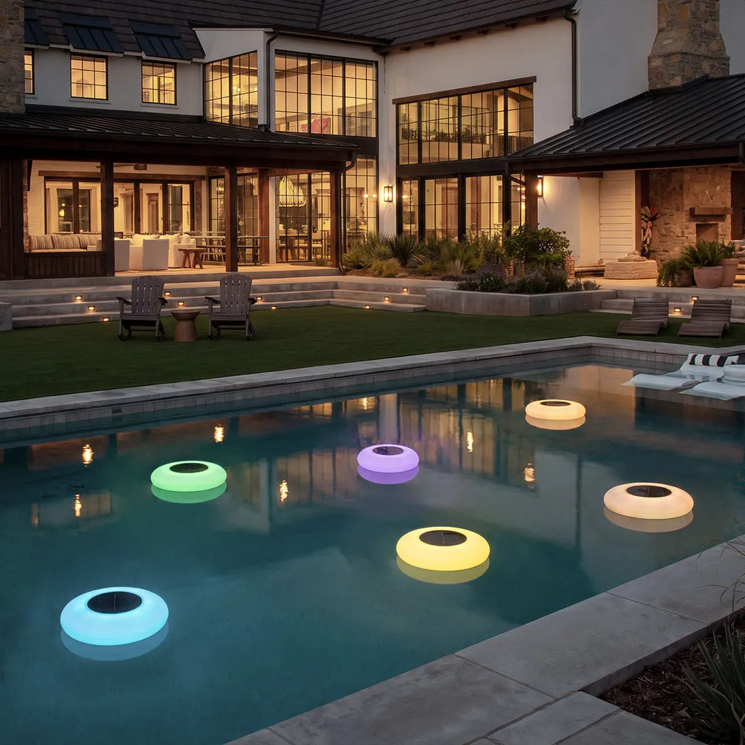 Floating pond lamps drifting across a residential pool, creating colorful illuminated accents for outdoor water feature lighting.