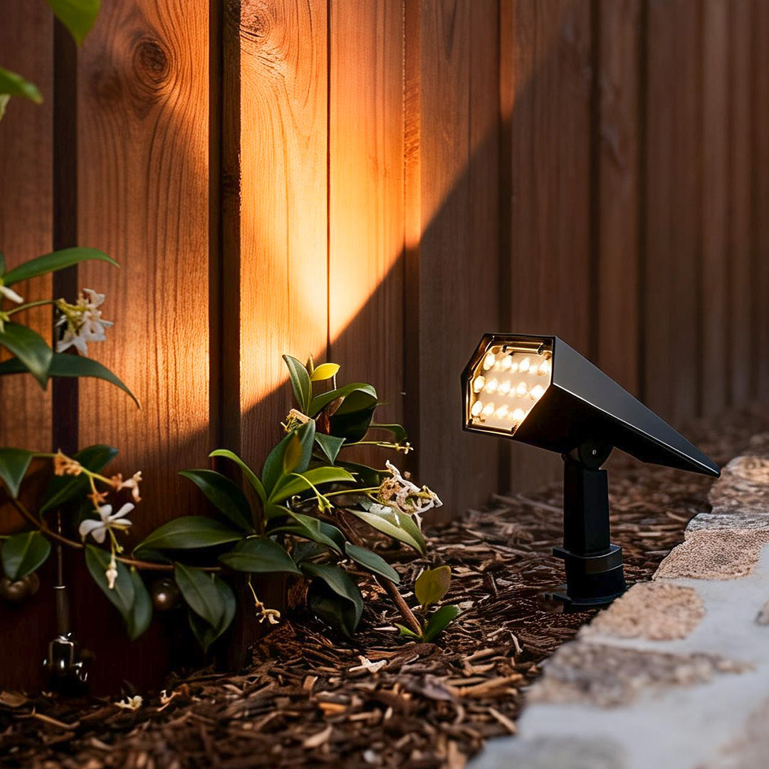 Flood spike light mounted near wooden fence casting bright warm light on green shrubs for evening garden ambiance.