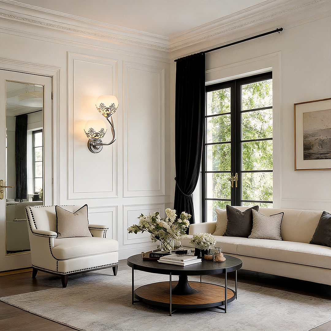 Pair of floral wall sconces lighting a bright traditional living room with large windows.