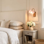 Flower wall light mounted above a bedside table with a pink glass floral shade in a cozy bedroom.